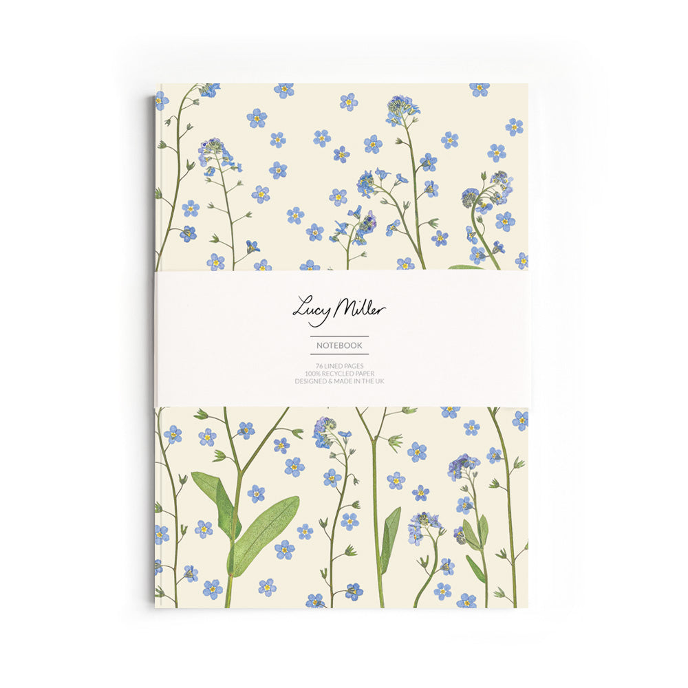 Notebook with pressed forget-me-not floral design with a belly band featuring 'Lucy Miller' branding. On a white background.