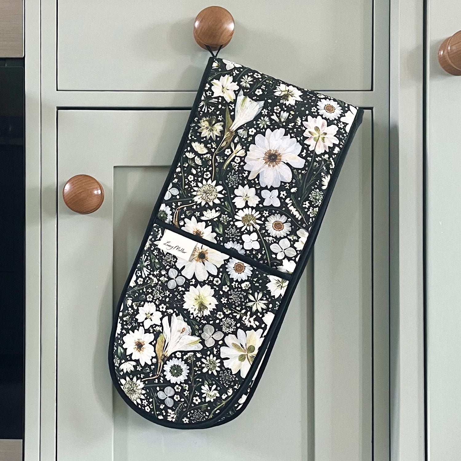 Double oven gloves with pressed white flower design on a black background. Featuring a black hanging loop for easy storage.
