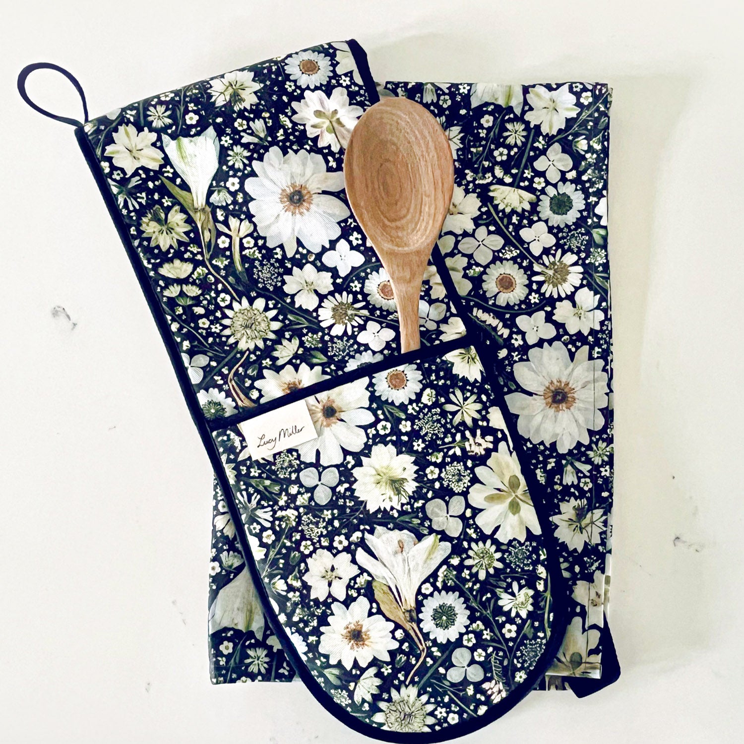 A kitchen gift set comprising of stylish double oven mitts and a matching tea towel. With a unique pressed white flower design on a black background. The perfect gift for bakers, chefs, and cooks.