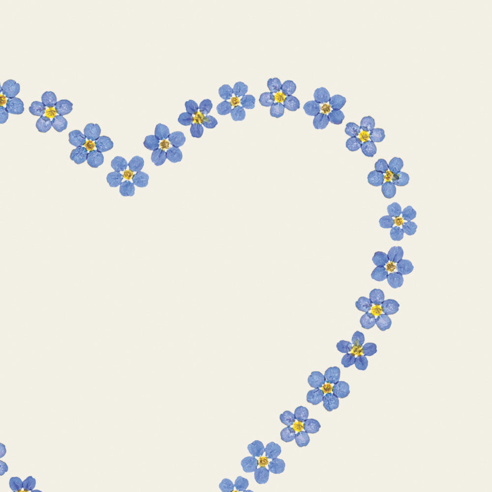 Close up of greetings card with a love heart made of pressed blue forget-me-not flowers on an off-white background.