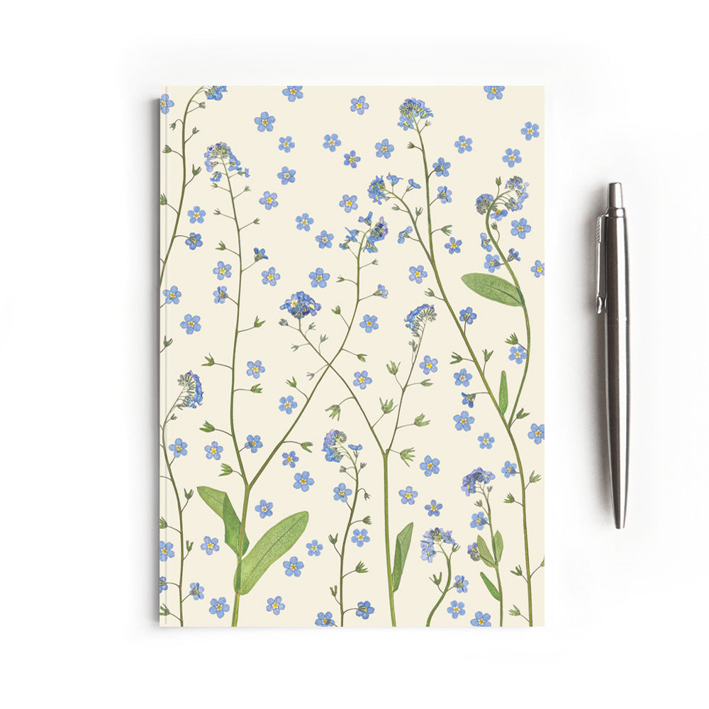 Notebook with pressed forget-me-not floral design on a white background and styled with a pen
