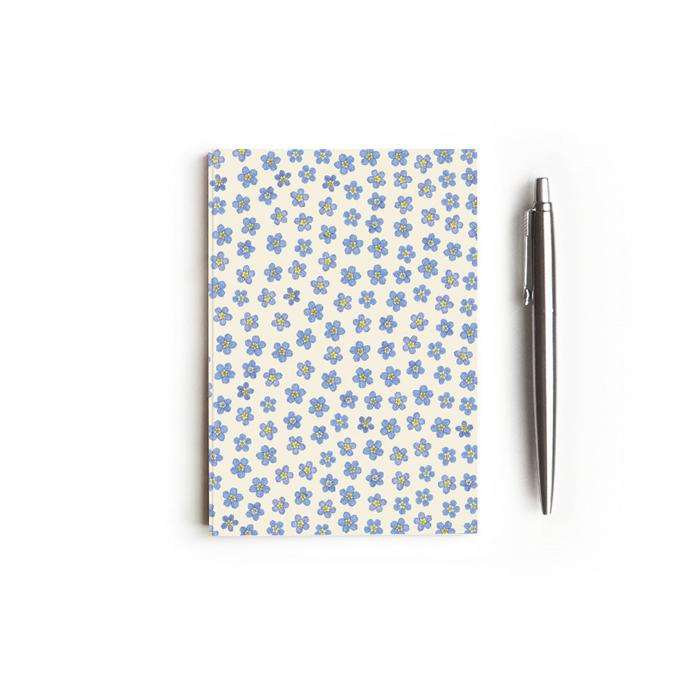 Notebook with blue forget-me-not pattern on a white background, styled with a pen.
